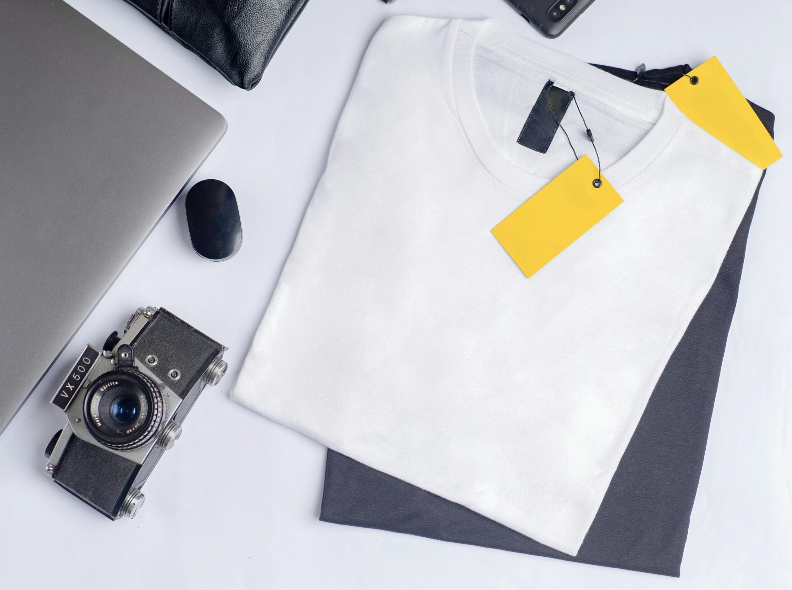 Stylish flat lay featuring a vintage camera, clothing, and laptop on a clean white background.